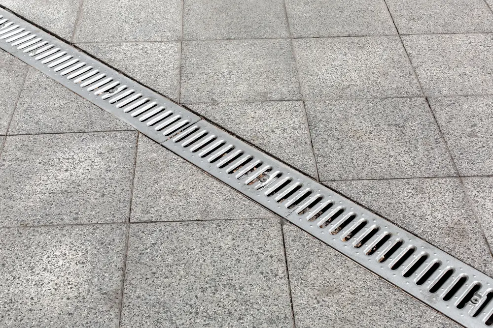 Trench drain gray with steel purification grate on granite stone tile road improvement of the city, close up details drainage system