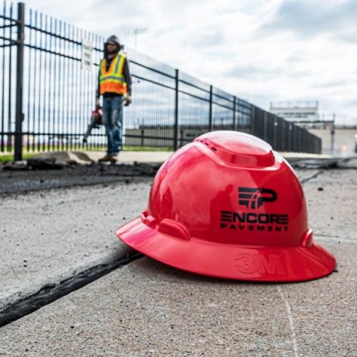 Encore Pavement hard hat sitting on concrete featuring company logo.
