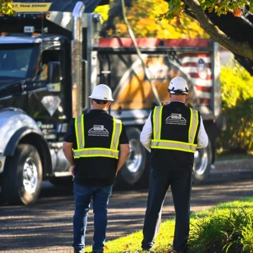Two Eosso Brothers Paving employees from behind stand on sidewalk watching jobsite.